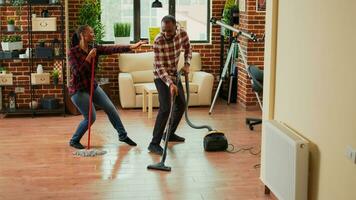 Jeune content couple écoute à la musique et la lessive planchers dans appartement, Faire idiot Danse se déplace. de bonne humeur gens Faire printemps nettoyage et dansant, éponger carrelage. ordinateur de poche tir. photo