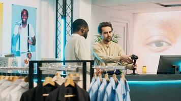 africain américain homme payant pour Nouveau moderne vêtements, fabrication transaction sur pos Terminal dans achats centre. Masculin client parlant à boutique assistant à en espèces enregistrer, commercial activité. ordinateur de poche tir. photo