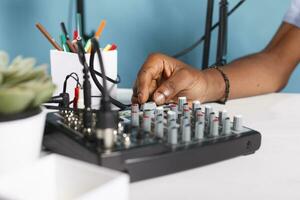 homme main tournant bouton sur du son manette équipement dans studio proche en haut. africain américain blogueur en utilisant la musique mixer console professionnel équipement tandis que création numérique contenu pour vlog photo