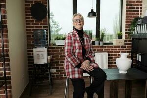 portrait de positif souriant Sénior femme expérimenté et Créatif art prof séance sur table avec céramique vase et souriant à caméra. de bonne humeur femelle artiste dans studio, enseignement encore la vie dessin photo