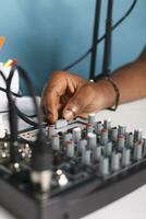 homme bras tournant bouton casquette sur le volume manette dans blogueur studio proche en haut. africain américain vlogger en utilisant du son mixer station professionnel équipement tandis que création la toile contenu photo