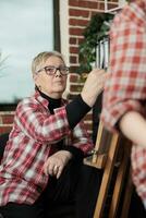 mature femme apprentissage à dessiner, retraité Dame en portant crayon, dessin sur chevalet et écoute à professeur, développement artistique compétences dans retraite. Créatif loisirs et art thérapie pour les personnes âgées photo