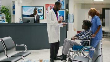 infirmière portion africain américain patient avec invalidité, en train de préparer Masculin fauteuil roulant utilisateur pour vérification visite avec médecin. la personne transaction avec chronique déficience visite santé centre. photo