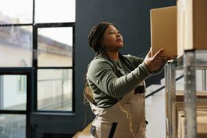 africain américain employé en mettant des produits dans carton des boites, en train de préparer les clients ordres dans entrepôt. espace de rangement pièce superviseur travail à paquets livraison tandis que Faire des biens qualité contrôle photo