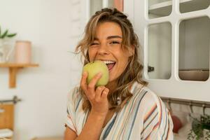 marrant femme en mangeant Pomme sur cuisine.régime en bonne santé mode de vie concept. photo