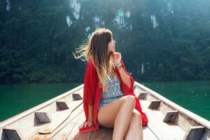 une sexy Jeune femme portant une bikini est séance sur une petit bateau près une tropical île. été vacances. photo