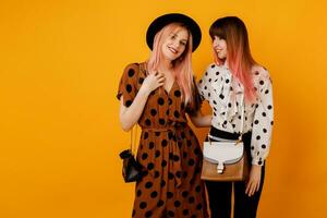 deux amis, jolie les filles en marchant et ayant amusement sur Jaune Contexte dans studio. content femme avec rose Cheveux avec sa blond ami ayant génial temps. photo