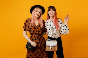 deux amis, jolie les filles en marchant et ayant amusement sur Jaune Contexte dans studio. content femme avec rose Cheveux avec sa blond ami ayant génial temps. photo