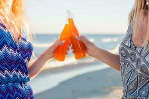 été vacances et vacances concept. copains en buvant limonade ou de l'alcool , en portant boisson dans bouteilles. profiter le coucher du soleil sur le plage. fête temps. concentrer sur bouteille. photo