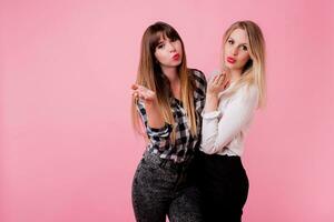 deux souriant femmes étreindre et permanent isoler plus de rose Contexte . brunette et blond filles. Naturel faire en haut. photo