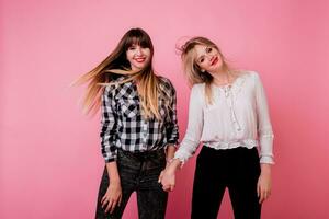 deux espiègle femmes sauter et ayant amusement dans studio sur rose Contexte. venteux Cheveux. positif ambiance. photo