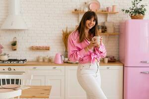 élégant brunette femme enjoing confortable Matin avec tasse de thé dans lumière moderne cuisine. photo