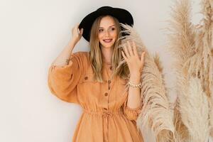 élégant femme dans été tenue posant plus de blanc Contexte dans studio avec pampa herbe décor. portant lin robe. photo