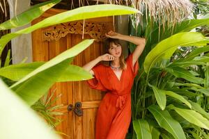 magnifique brunette femme dans élégant été tenue enjoing vacances dans luxe station balnéaire. exotique jardin avec tropical les plantes. photo