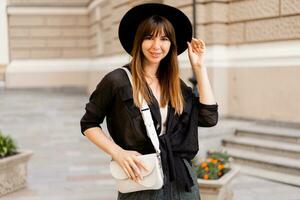 proche en haut portrait de élégant brunette femme dans décontractée tenue et noir chapeau. enjoing vacances dans européen ville. photo