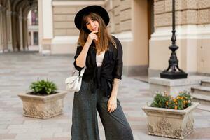 rue mode photo de élégant brunette femme dans décontractée tenue et noir chapeau. enjoing vacances dans européen ville.