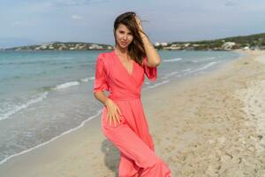 séduisant brunette femme avec tatoo sur main dans rose robe posant sur le plage. photo