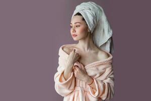 artistique souriant Jeune femme portant peignoir de bain et serviette plus de sa tête permanent plus de rose Contexte violet Contexte. photo