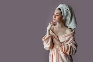 artistique souriant Jeune femme portant peignoir de bain et serviette plus de sa tête permanent plus de rose Contexte violet Contexte. photo