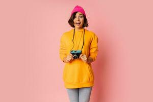 femme dans rose chapeau et Orange sweat à capuche avec surprise visage en utilisant photo caméra sur rose antécédent.