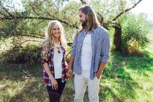 romantique branché couple en marchant dans ensoleillé été parc, chaud temps. Beau homme avec barbe et jolie mignonne blond femme profiter marcher. photo