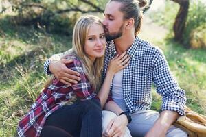 proche en haut portrait de romantique couple étreindre et séance dans parc , portant plaid chemise . Jeune blond fille avec sa Beau copain avec barbe profiter ensoleillé printemps journée . ancien couleurs. photo