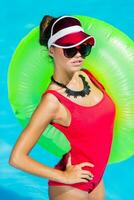 sexy bronzé femme dans rouge maillot de bain ayant amusement et profiter été dans incroyable gros nager bassin. élégant transparent casquette. plage faire la fête. photo