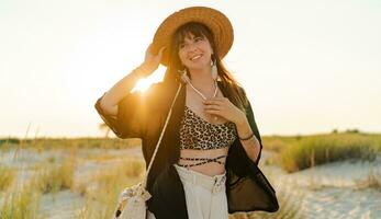 content européen femme dans élégant boho été porter en marchant sur le plage. chaud le coucher du soleil couleurs.paille chapeau. photo