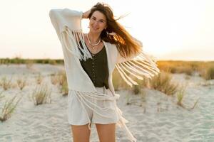 été ambiance. espiègle brunette femme dansant dans lumière du soleil sur le plage. boho style. branché collier et des boucles d'oreilles. photo