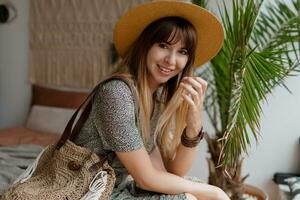 femme séance sur lit dans sa boho appartements. élégant décor, Accueil les plantes. confortable temps. photo