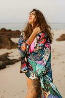 Extérieur photo de de bonne humeur magnifique brunette femme dans sexy rose maillots de bain posant sur le plage dans le coucher du soleil lumière. parfait ondulé Cheveux, bronzer parcourir corps. été tropical ambiance.