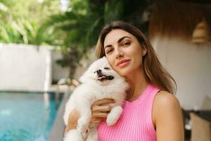 adorable jouet poméranien chien dans bras de ses aimant propriétaire. petit adorable chienchien avec marrant fourrure avec jolie femme. tropical moder villa sur Contexte. photo