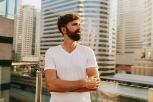 portrait de Beau sur de soi élégant Masculin. moderne homme habillé dans blanc chemise. mode Masculin posant dans le rue Contexte près grattes ciels dans des lunettes de soleil. en plein air à le coucher du soleil photo