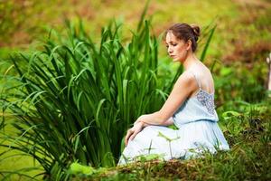 jeune femme dans une robe bleue est assise sur l'herbe