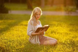 fille assise sur l'herbe et lisant un livre photo