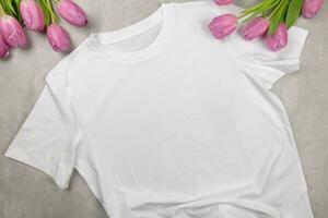 blanc aux femmes coton T-shirt maquette avec rose tulipes. conception t chemise modèle, impression présentation moquer en haut. Haut vue plat poser. béton pierre Contexte. photo