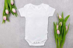 blanc bébé fille ou garçon le maillot de corps maquette plat allonger avec rose tulipes fleurs sur le gris béton Contexte. conception grenouillère modèle, impression présentation moquer en haut. Haut voir. photo