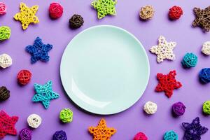 vue de dessus de l'assiette de vacances décorée de boules tricotées et d'étoiles sur fond coloré. décorations et jouets du nouvel an. concept de dîner de noël en famille photo