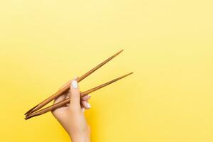 main féminine avec des baguettes sur fond jaune. cuisine asiatique traditionnelle avec espace vide pour votre conception photo