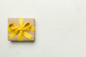 vacances cadeau boîte enveloppé dans artisanat papier avec coloré arc sur table Contexte. Haut voir, plat poser, copie espace photo