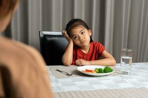 mère est récit sa mignonne enfant manger utile des légumes mais le enfant refuse à manger. photo