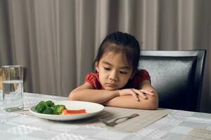 peu mignonne enfant fille refusant à manger en bonne santé des légumes. les enfants faire ne pas comme à manger des légumes. photo