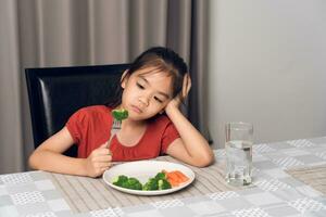 peu mignonne enfant fille refusant à manger en bonne santé des légumes. les enfants faire ne pas comme à manger des légumes. photo