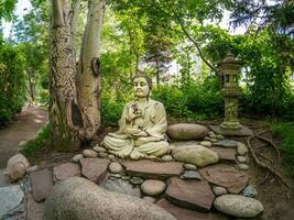 pierre Gautama Bouddha décoratif statue dans une jardin en dessous de vert feuilles. Extérieur jardin décor concept. abakan photo