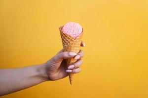 crème glacée dans une tasse de gaufres dans une main féminine sur fond jaune photo