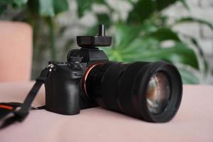 appareil photo noir avec un objectif sur un fond flou de feuilles vertes.