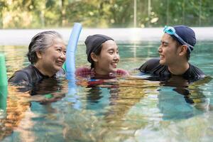 Jeune entraîneur portion Sénior femme dans aqua aérobie et travail en dehors dans le bassin. vieux femme et mature homme Faire aqua aérobie exercice dans nager piscine, personnes âgées des sports, et actif mode de vie concept. photo