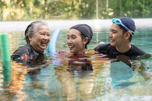 Jeune entraîneur portion Sénior femme dans aqua aérobie et travail en dehors dans le bassin. vieux femme et mature homme Faire aqua aérobie exercice dans nager piscine, personnes âgées des sports, et actif mode de vie concept. photo