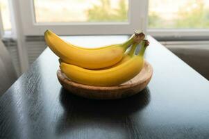 mûr Jaune fruit bananes sur en bois assiette sur tableau. foncé Contexte contre la fenêtre. en bonne santé tropical nourriture photo