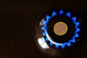 Brûleur de cuisinière à gaz avec une pièce en euros posée sur le dessus, brûlant du gaz naturel avec une flamme bleue photo